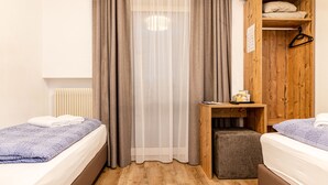 Een slaapkamer met twee bedden, een houten garderobe, een klein tafeltje met spullen en een radiator.