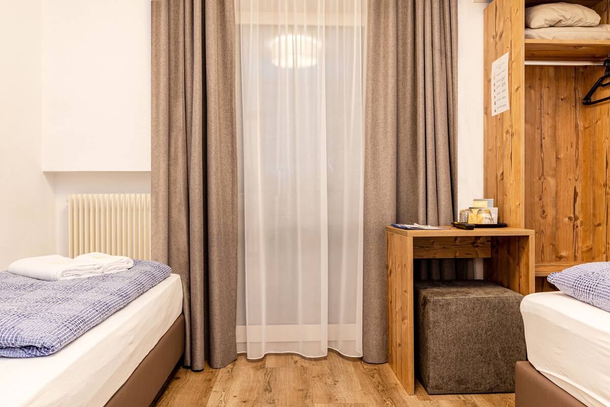 Un dormitorio con dos camas, un armario de madera, una mesita con objetos y un radiador.
