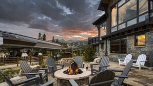 A stone fire pit surrounded by Adirondack chairs, with a mountain view and a building with large windows and stone walls. - Closest to Gondola | Shock Hill Majestic | Views! (Breckenridge)