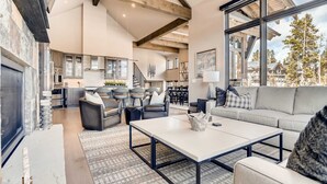 A spacious living area with a large window, a fireplace, and a modern kitchen in the background. - Closest to Gondola | Shock Hill Majestic | Views! (Breckenridge)