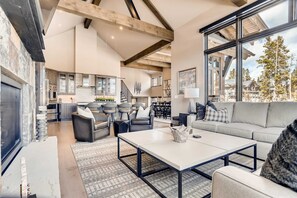Een ruime woonkamer met een groot raam, een open haard en een moderne keuken op de achtergrond.