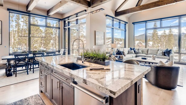 A spacious kitchen with a large island, wooden beams, and large windows offering a view of trees and mountains. - Closest to Gondola | Shock Hill Majestic | Views! (Breckenridge)