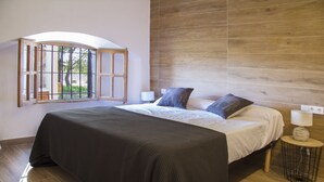 A bedroom with a large bed, a window with a view of trees, a wooden headboard, and a bedside table with a lamp. - Finca Sa Caseta Biniali (Sencelles)