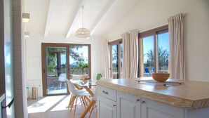 A modern kitchen with a large island, wooden chairs, and a view of the outdoors. - Finca Sa Caseta Biniali (Sencelles)