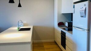 Une cuisine de taille réduite, dotée d’un plan de travail blanc, d’un évier, d’un grille-pain et d’un réfrigérateur.