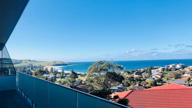 Une vue sur la côte depuis un balcon doté d’un toit rouge, donnant sur une plage et l’océan.