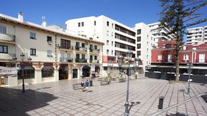 A plaza with tiled flooring, benches, and street lamps. There are buildings with balconies and storefronts in the background. - MONKÓ KIWI TROPYCAL APARTMENT (Torremolinos)