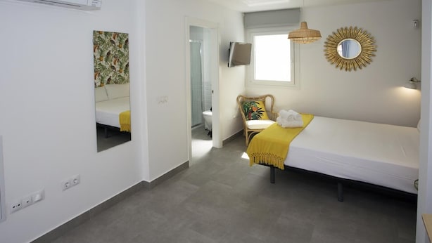 A hotel room with a bed, a chair, a small table, a mirror, and a window. - MONKÓ KIWI TROPYCAL APARTMENT (Torremolinos)