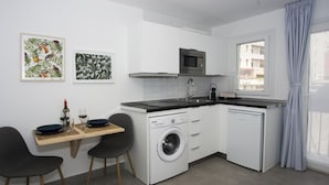 A compact kitchen with a washing machine, a microwave, and a sink. There is a dining area with a table and chairs. - MONKÓ KIWI TROPYCAL APARTMENT (Torremolinos)