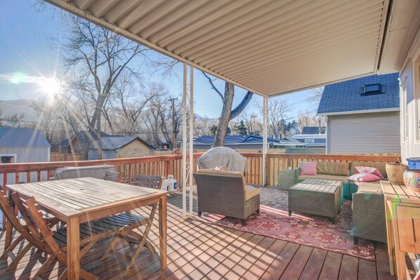 A covered deck with a wooden table and chairs, a grill, and wicker furniture.