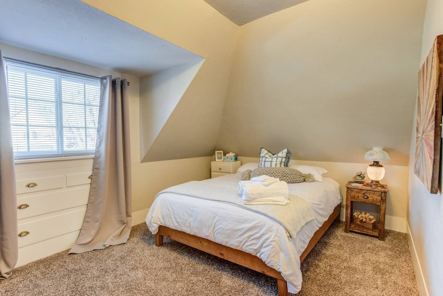 A bedroom with a bed, a nightstand, a dresser, and a window with curtains.