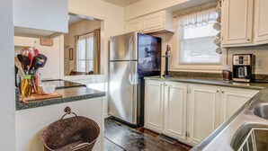 A compact kitchen with white cabinets, a stainless steel refrigerator, a coffee maker, and a window with blinds. - 1893 Classic 4 Blocks From Great Dining & Shops (Colorado Springs)