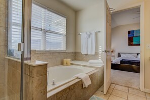 Une salle de bain moderne avec une baignoire, une douche à l’italienne en verre et une grande fenêtre équipée de stores.