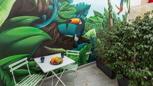 A mural of a toucan on a tree, a table with fruit, and a potted plant. - MONKÓ LEMON TROPYCAL APARTMENT (Torremolinos)
