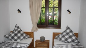 Een slaapkamer met twee enkele bedden, een nachtkastje, een raam met uitzicht op groen en een gordijn.