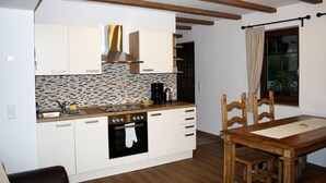 Een kleine keuken met witte kastjes, een betegelde spatwand en een houten eettafel.