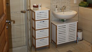 Een badkamer met een douchecabine van glas, een wastafel met spiegel erboven en een kleine prullenbak.
