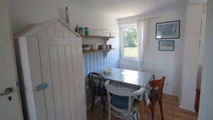 A dining area with a table and chairs, a window with curtains, and a view of greenery outside. - Maisonettewohnung am Privatsee (Karlsruhe)