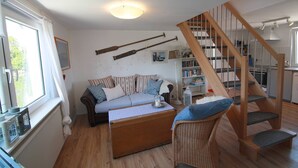 A cozy living room with a sofa, a wooden chair, a staircase, and a bookshelf. - Maisonettewohnung am Privatsee (Karlsruhe)