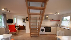 A modern kitchen with a washing machine, a dining area with a red chair, and a wooden staircase. - Maisonettewohnung mit großer Terrasse (Karlsruhe)