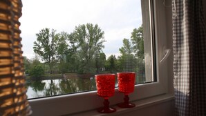 A window with two red glasses on a sill, overlooking a body of water and trees. - Maisonettewohnung mit großer Terrasse (Karlsruhe)