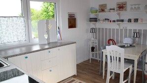 A compact kitchen with white cabinetry, a dining table with chairs, and a window with curtains. - Maisonettewohnung mit großer Terrasse (Karlsruhe)