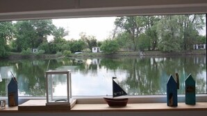 A view through a window with a small sailboat model, a framed picture, and decorative houses on a ledge. - Schnuckliges Appartement am Seeufer (Karlsruhe)