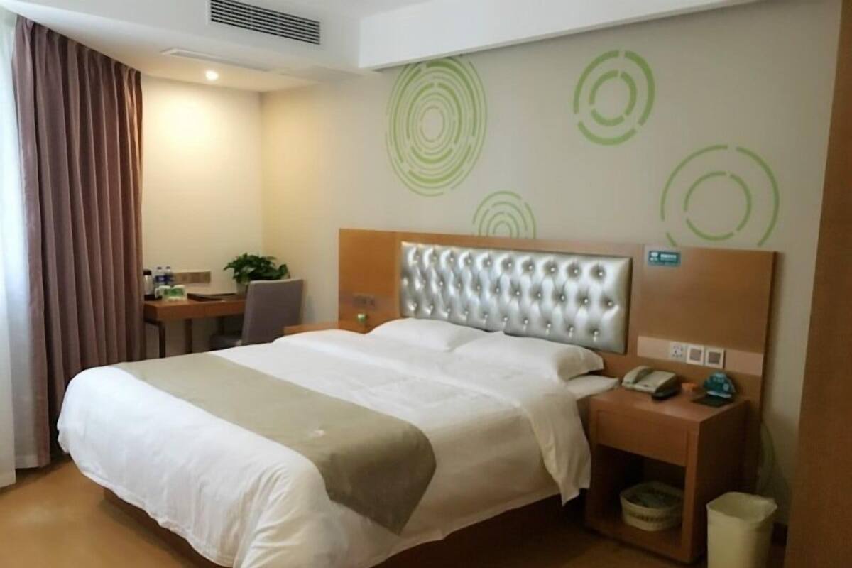 Een hotelkamer met een groot bed, een bureau, een stoel, een nachtkastje met een lamp en een prullenbak.