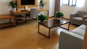 Una sala de estar moderna con piso de madera, una mesa de centro de vidrio, un sofá gris, un televisor montado en la pared y dos plantas en macetas.
