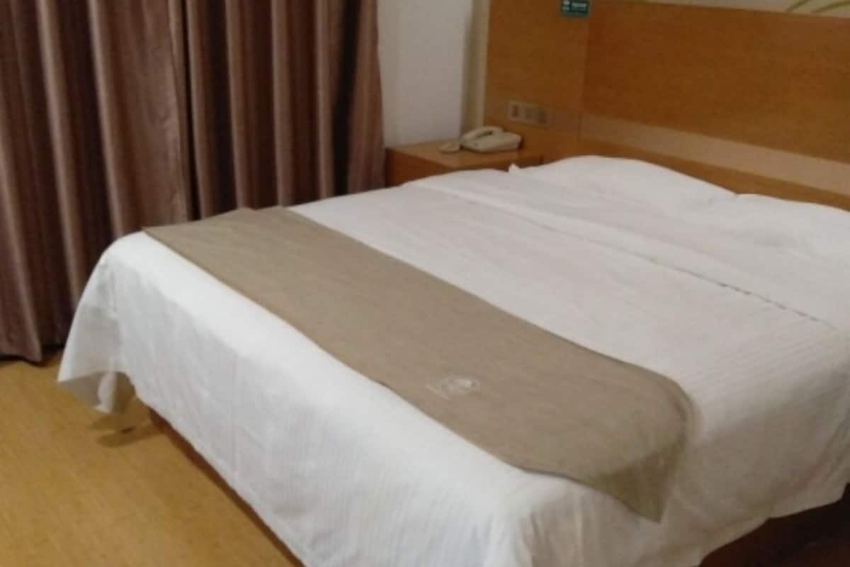 Een hotelkamer met een bed, nachtkastje, telefoon en gordijn.