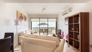 Ein Wohnzimmer mit einer Couch, einem Fernseher, einem Bücherregal und Blick auf die Stadt durch große Fenster.