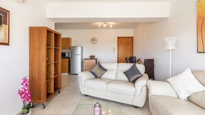 Ein Wohnzimmer mit einer Couch, einem Holzschrank, einem Kühlschrank, einer Mikrowelle und einem Essbereich mit Stühlen und einem Tisch.