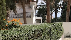 Ein angelegter Gartenbereich mit einer ordentlich geschnittenen Hecke, einem gefliesten Weg und einem Gebäude mit weißer Fassade und schwarzem Geländer.