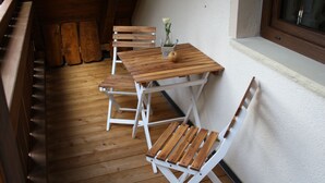 Un terrazzo in legno con tavolo e sedie, un vaso con un fiore e una finestra.