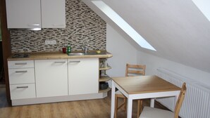 Una cucina compatta con mobili bianchi, un piano di lavoro in legno e un piccolo tavolo da pranzo con una sedia.