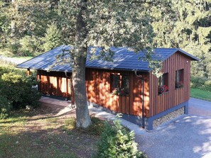Une cabane en bois avec un toit en pente, entourée d’arbres et bordée d’un chemin de gravier.