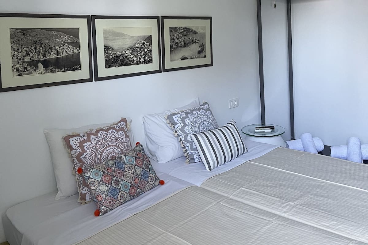 Una habitación de hotel con una cama, un ventilador de pie y tres fotografías en blanco y negro enmarcadas en la pared.
