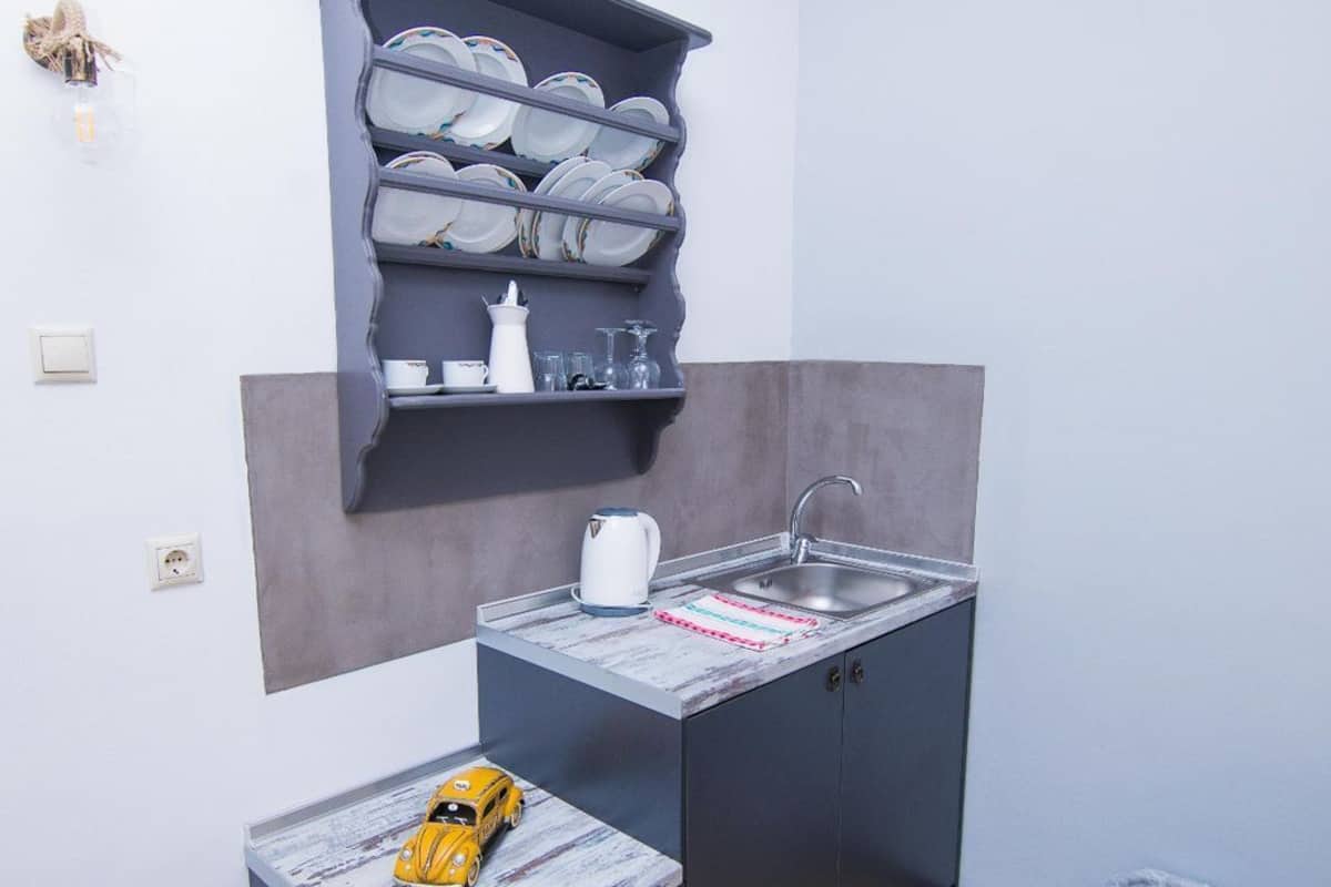 Cocina compacta con pileta integrada, una pequeña mesada y estante con platos y vasos.