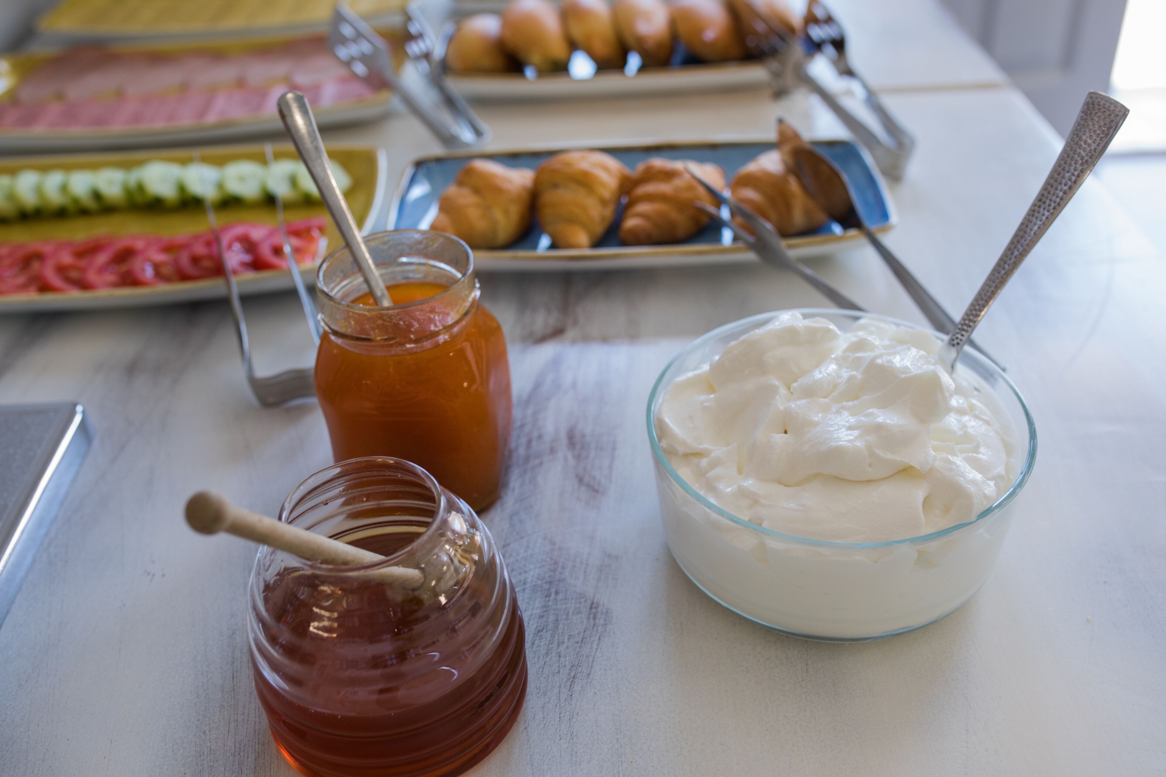Une table où l’on trouve une variété d’aliments, notamment un bol de yaourt, un pot de miel et des assiettes de pâtisseries.
