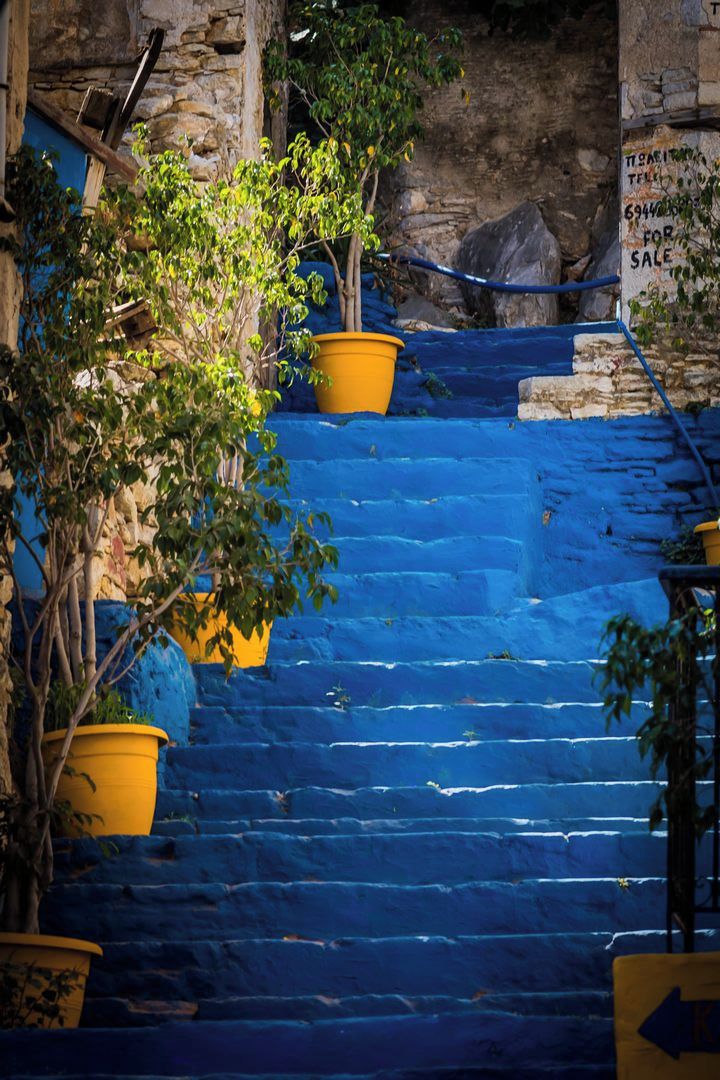 Unos escalones de color azul, macetas amarillas y un letrero que indica una propiedad en venta.