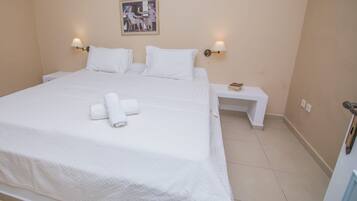 Una cama bien hecha con ropa blanca y toallas, dos mesitas de noche con lámparas y un cuadro en la pared.