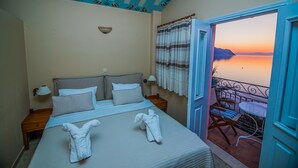 Ett hotellrum med en säng, två sängbord, ett litet bord, ett fönster med gardiner och en balkong med ett bord och stolar.