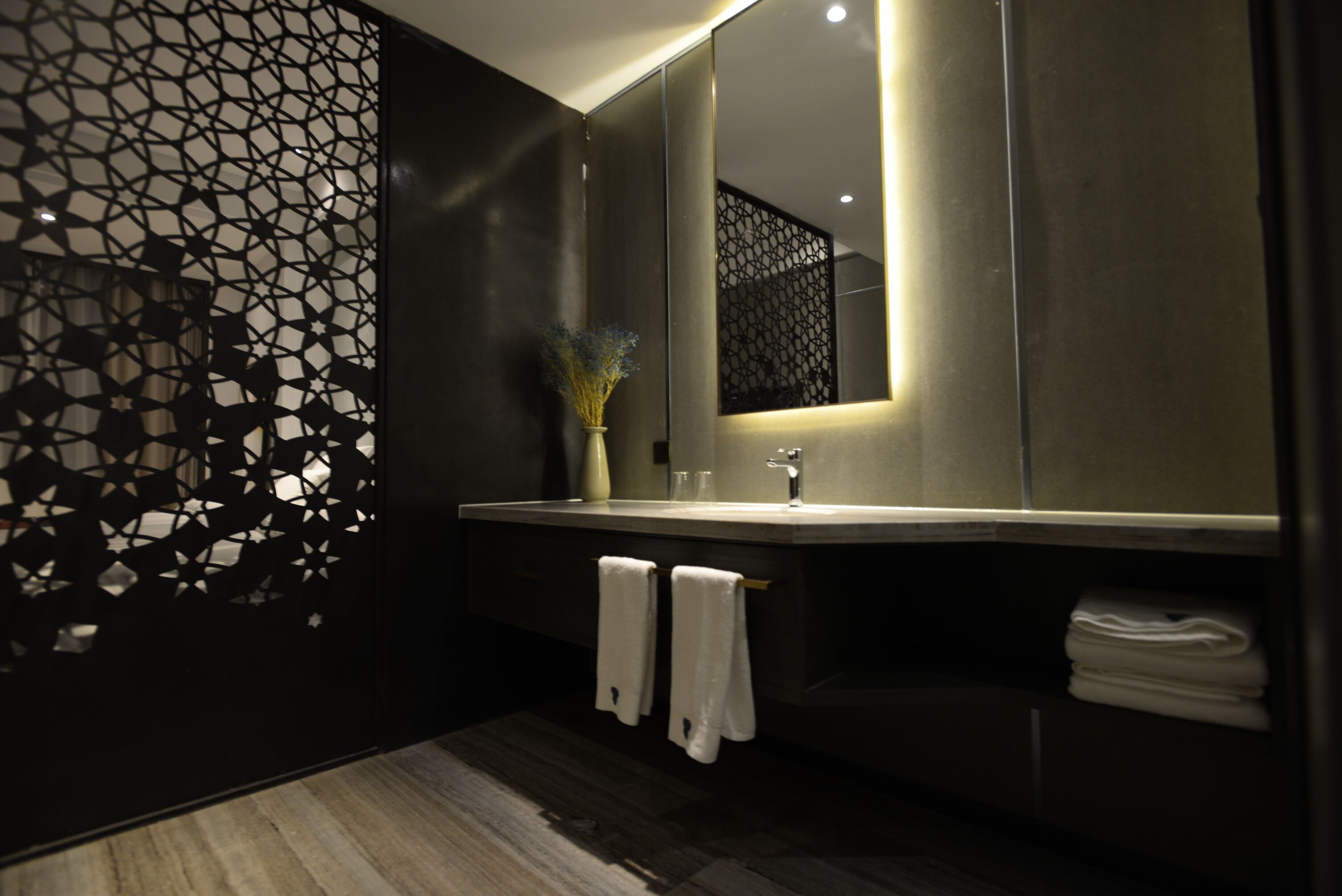 Une salle de bain moderne avec un grand miroir, un parquet en bois foncé et un panneau décoratif mural.
