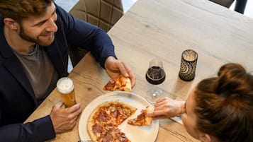 Uma mesa de jantar com pizza, copos de vinho e talheres.
