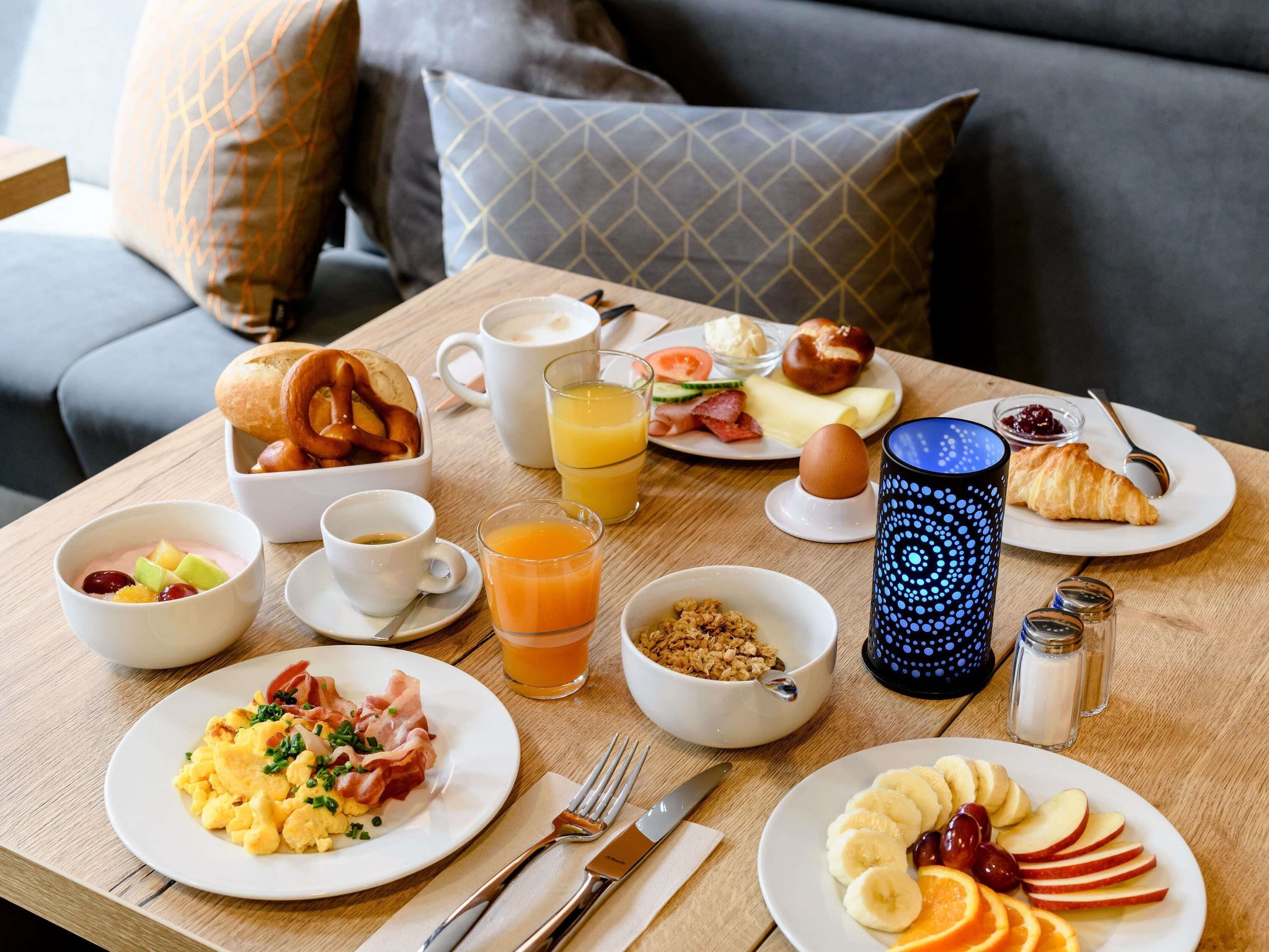 A breakfast table with plates of food, a coffee cup, a glass of orange juice, and a croissant.