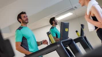 Un gimnasio con cintas de correr y un espejo grande.