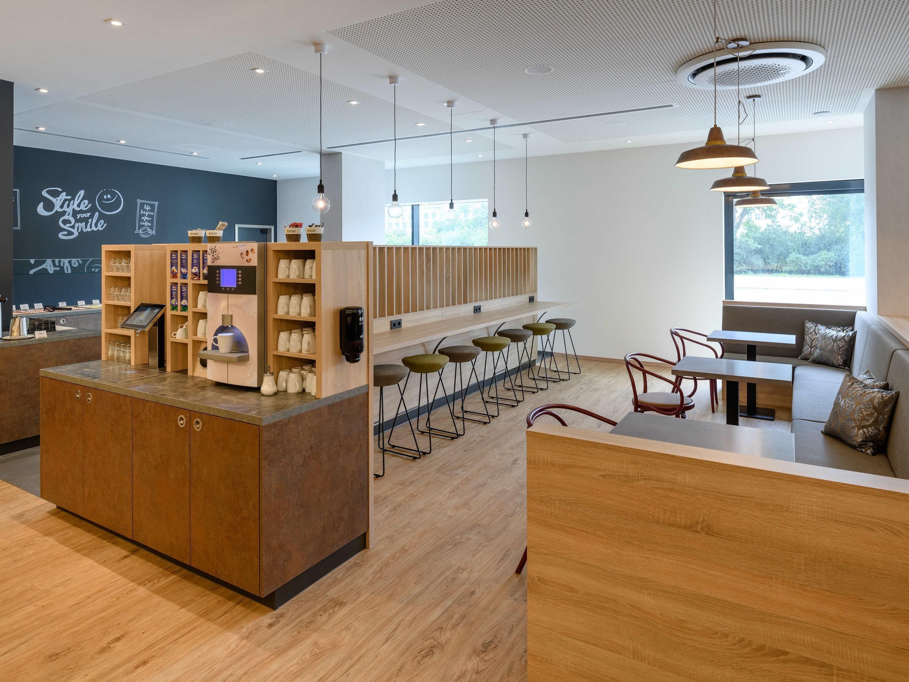 Um café moderno com balcão de madeira, banquetas e área de estar com sofá e mesa.