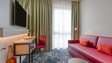 Een hotelkamer met een rode bank, een bureau met een flatscreen televisie, een stoel en een kamerbreed tapijt met dessin.