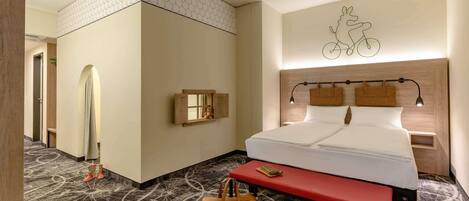 Quarto de hotel com cama, mesa de cabeceira, abajur e uma obra de arte de bicicleta na parede.