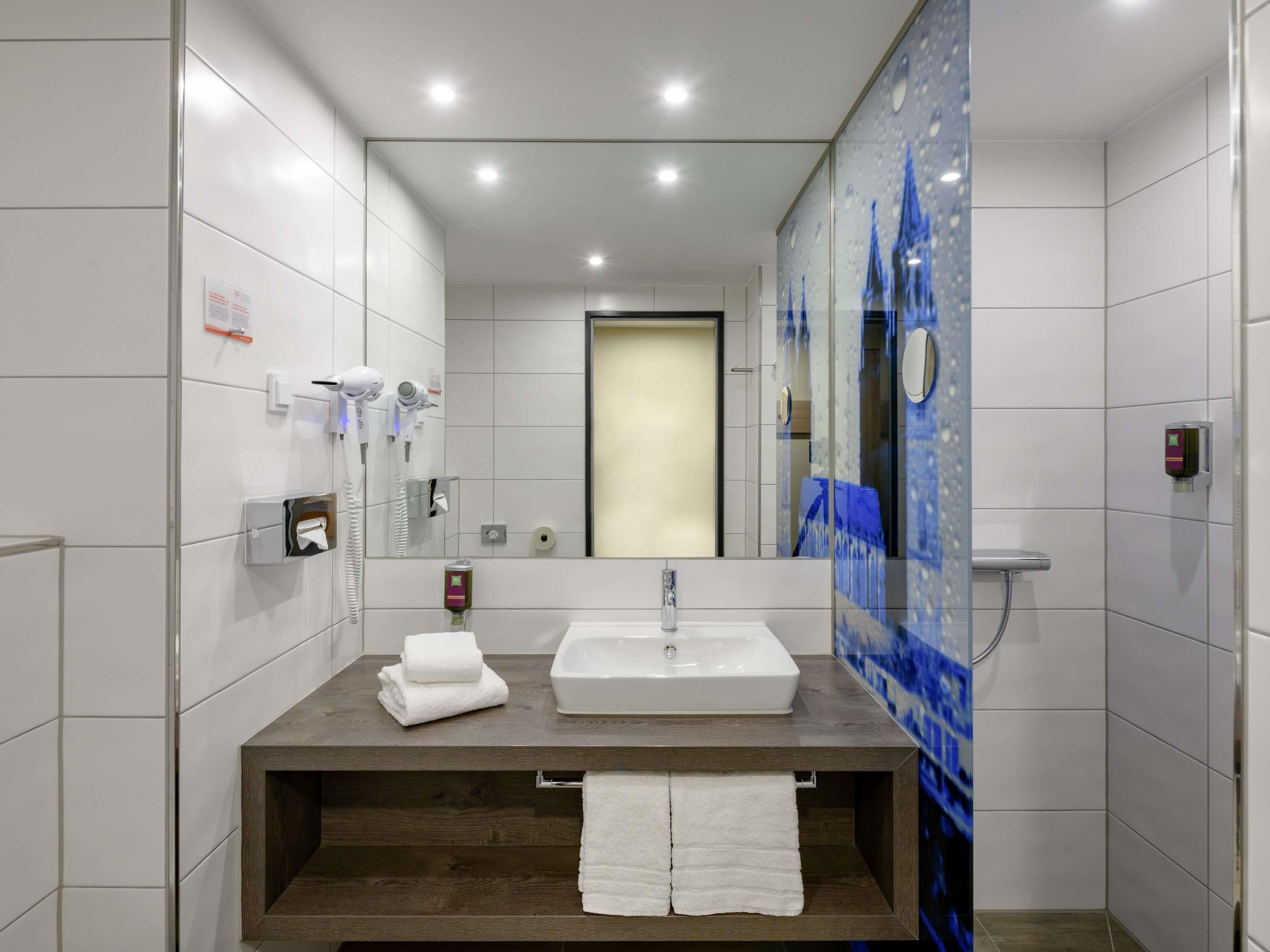 A modern bathroom with a large mirror, a sink, and a shower.